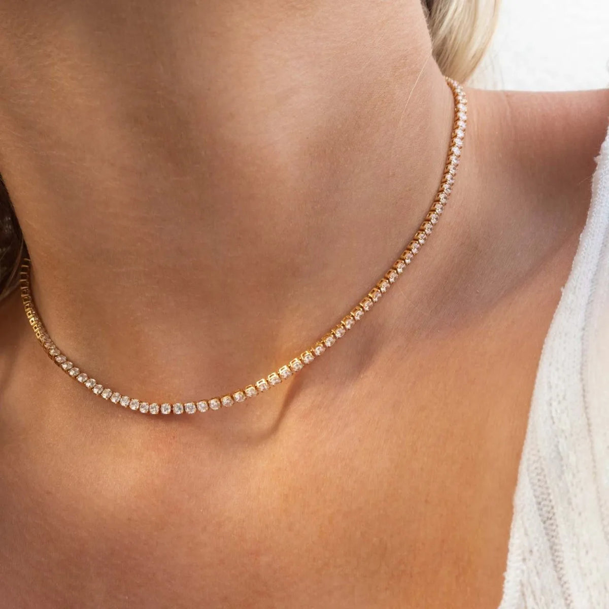 Primer plano de un collar tipo gargantilla dorado incrustado con pequeñas piedras claras, usado alrededor del cuello de una m