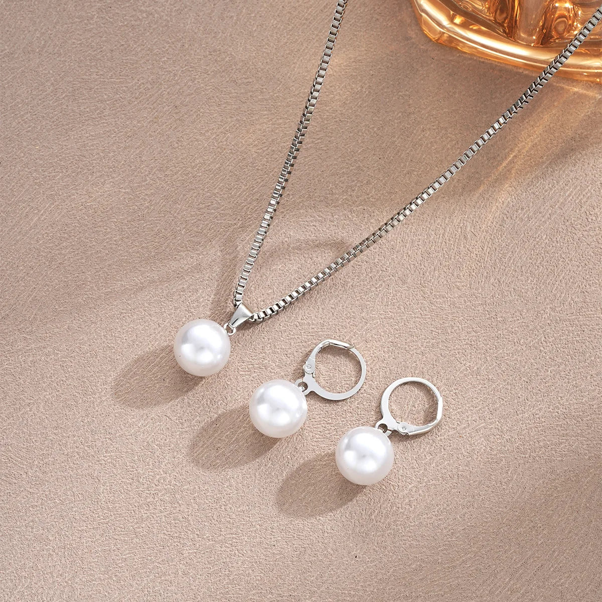 A delicate silver necklace with a pearl pendant and matching pearl hoop earrings displayed on a neutral background.