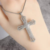 Silver cross amulet necklace with a detailed, textured design worn on a hand.