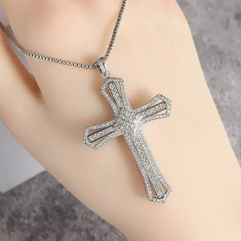 Silver cross amulet necklace with a detailed, textured design worn on a hand.