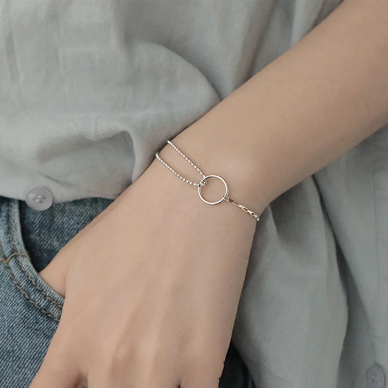 A close-up of a Sterling Silver double heart charm bracelet worn on a wrist against a light gray shirt.