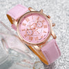 A pink fashion quartz wristwatch with a rose gold case and pink leather strap resting on a clear glass.
