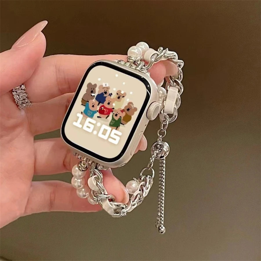 A hand holds a smartwatch with a beaded strap and charm, displaying the time 16:05.