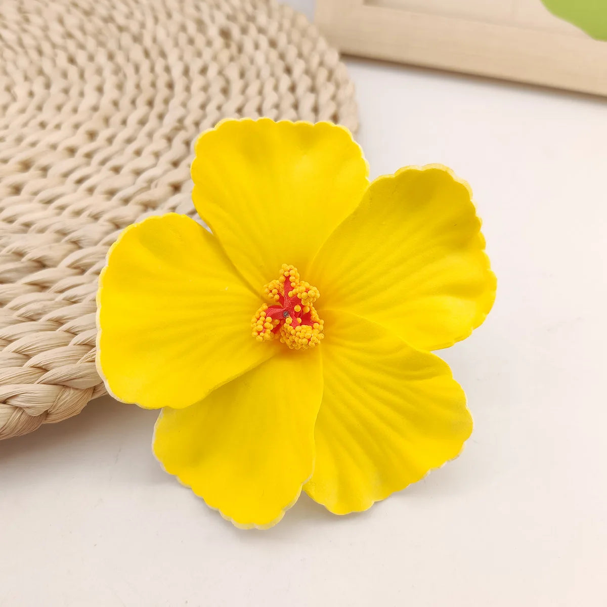 A bright yellow flower with a reddish center rests on a beige woven mat.
