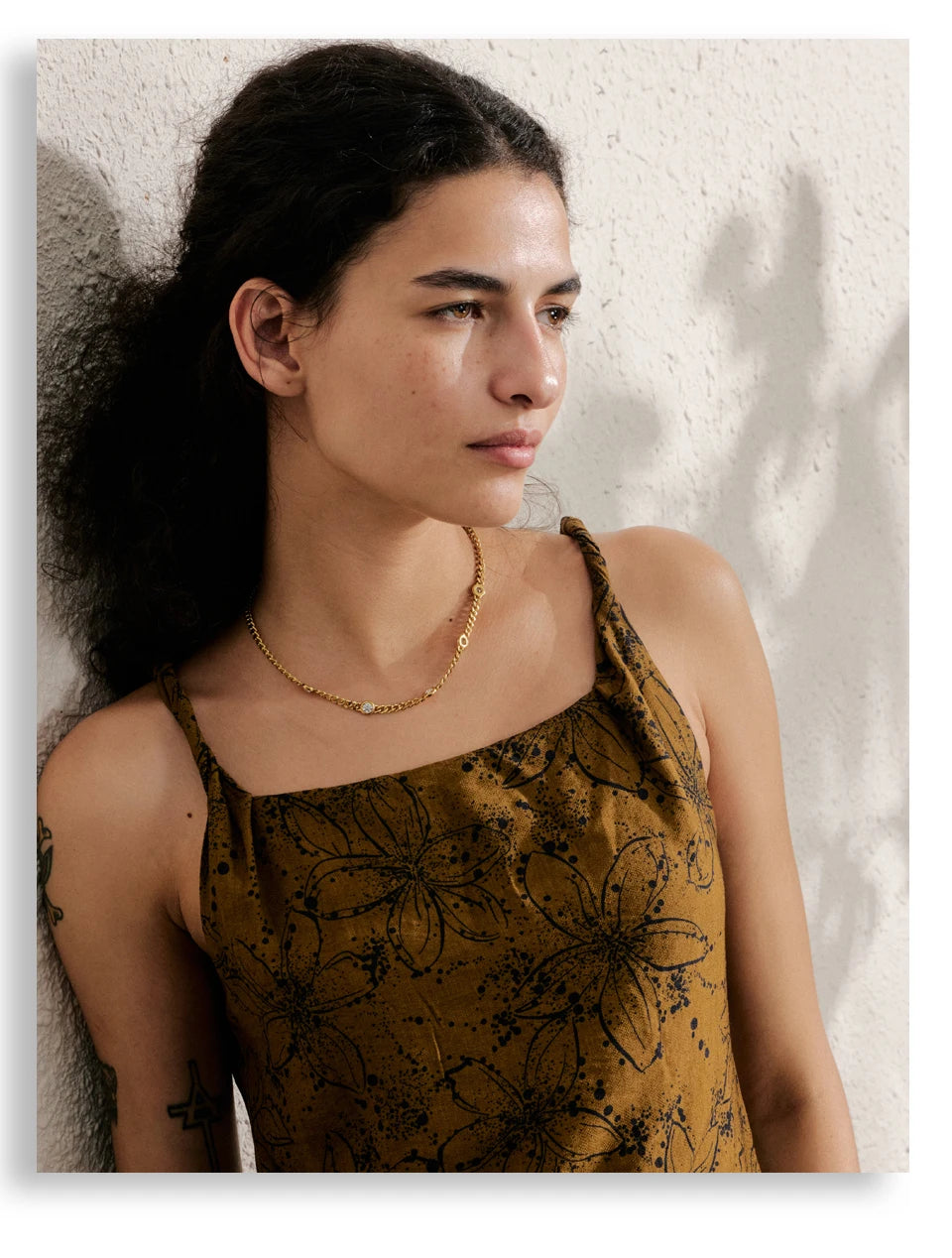 A woman wearing a gold stainless steel charm necklace with small CZ stones against a light background.