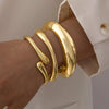 A hand wearing a stack of thick, gold, curved cuff bangles on the wrist.