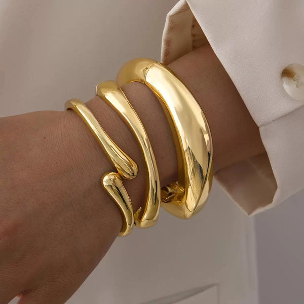 A hand wearing a stack of thick, gold, curved cuff bangles on the wrist.