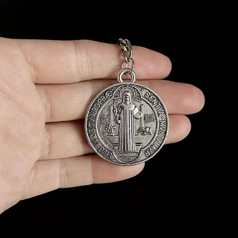A silver round medallion featuring a depiction of Christ and text, held in a person's hand.
