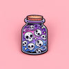 A dark purple enamel pin shaped like a skull with swirling patterns, set in a glass jar.