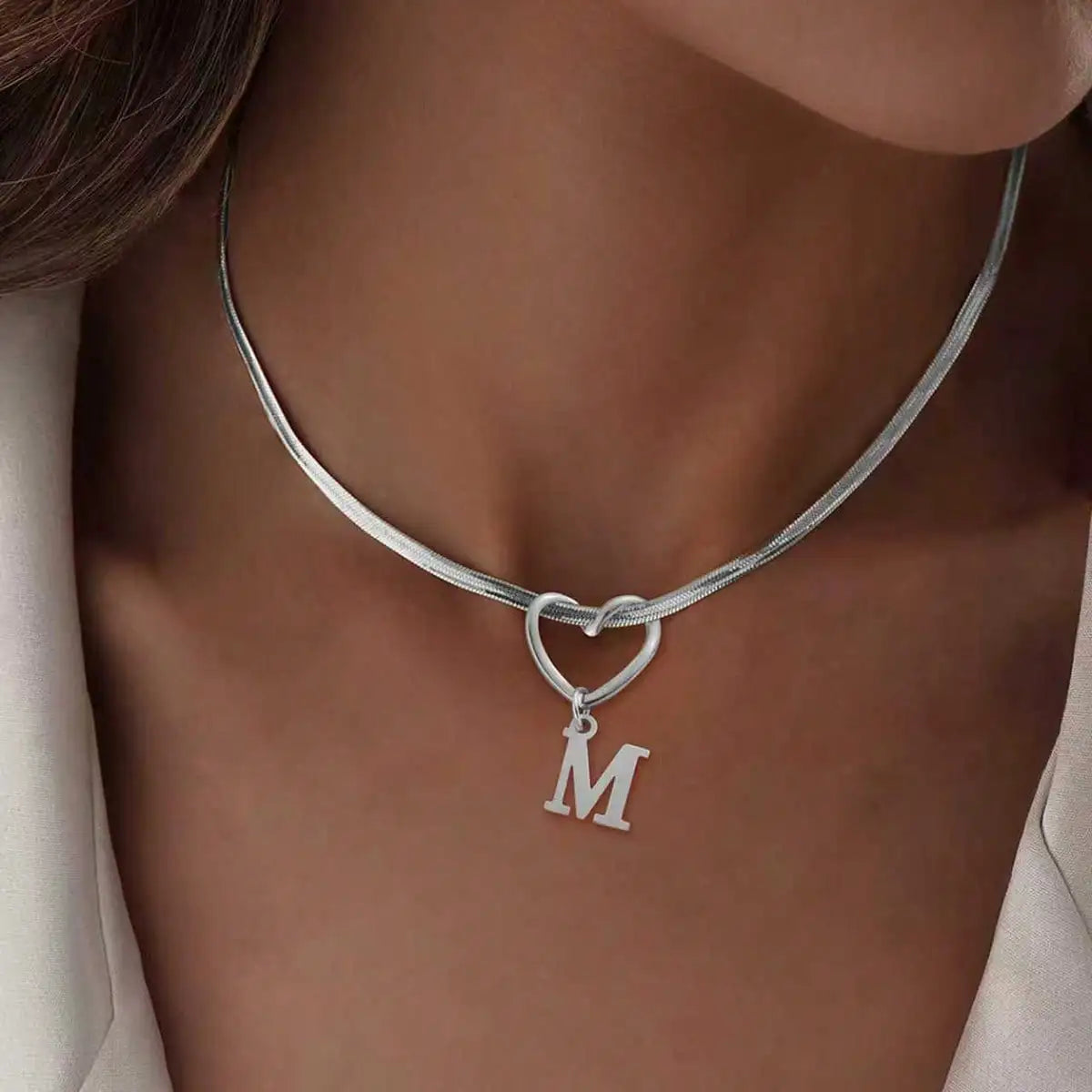 Nahaufnahme einer silbernen Herzkette mit einem Initialcharm, getragen um den Hals.
