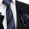 Schwarzes und blau gestreiftes Krawattentextil vor weißem Hemd und schwarzem Sakko mit dunkelblauer Blumenaccessoire.