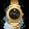 Reloj de cuarzo dorado con esfera negra, mojado por salpicaduras contra un fondo oscuro.