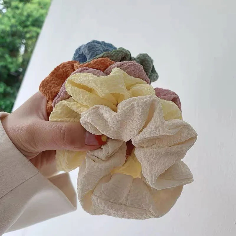 A hand holds a stack of colorful knitted hair scrunchie headbands in various shades of orange, yellow, and green.
