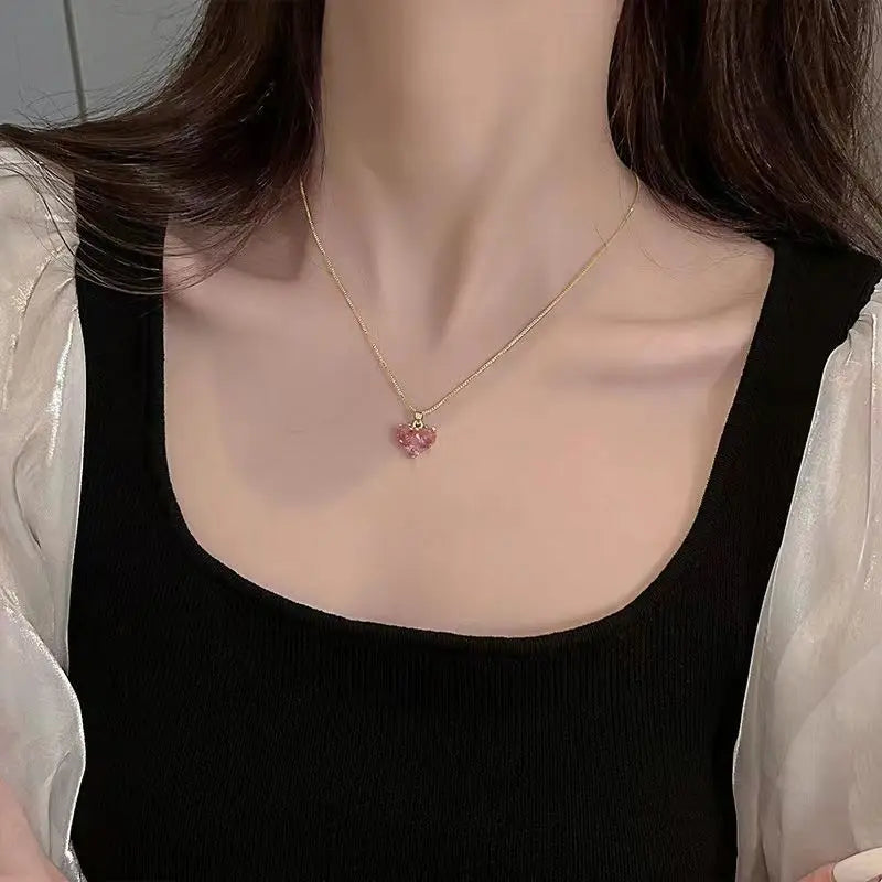 A close-up of a pink crystal heart necklace worn on a woman's neck against a dark top.