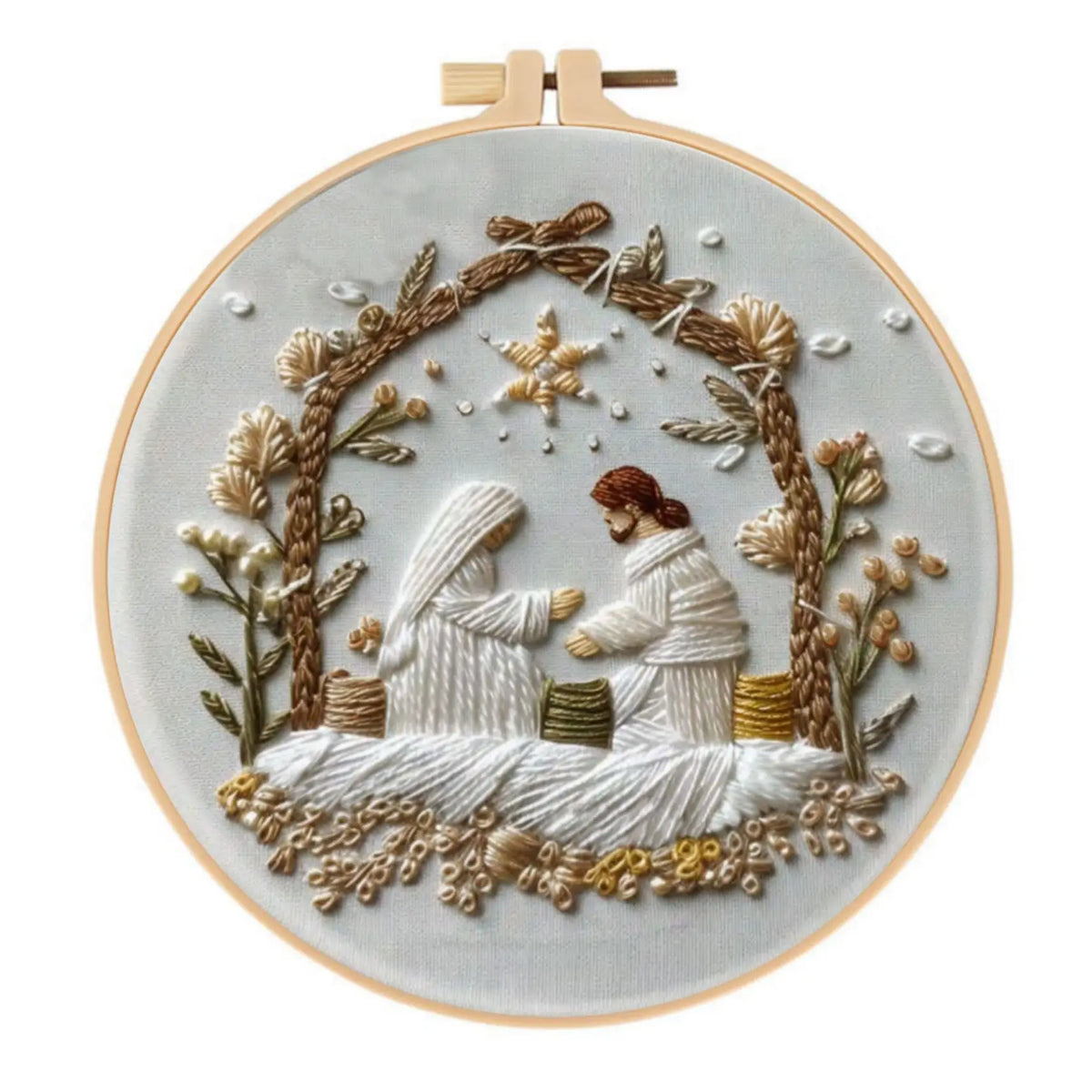 A white embroidery kit featuring a Christmas scene with two figures framed by branches and foliage.