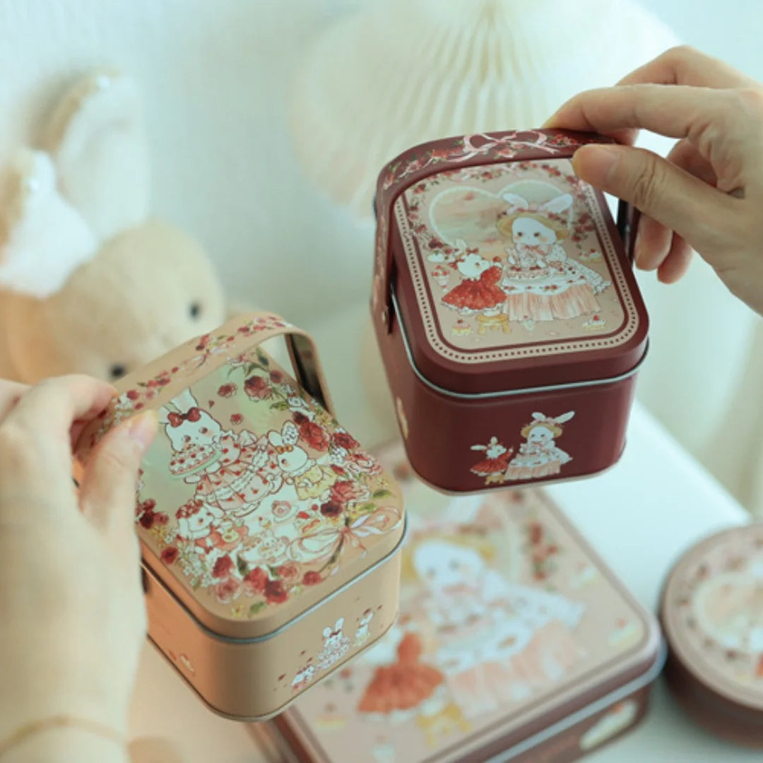 A hand is opening a decorative tinplate candy box with a carrying loop, revealing floral patterns inside.