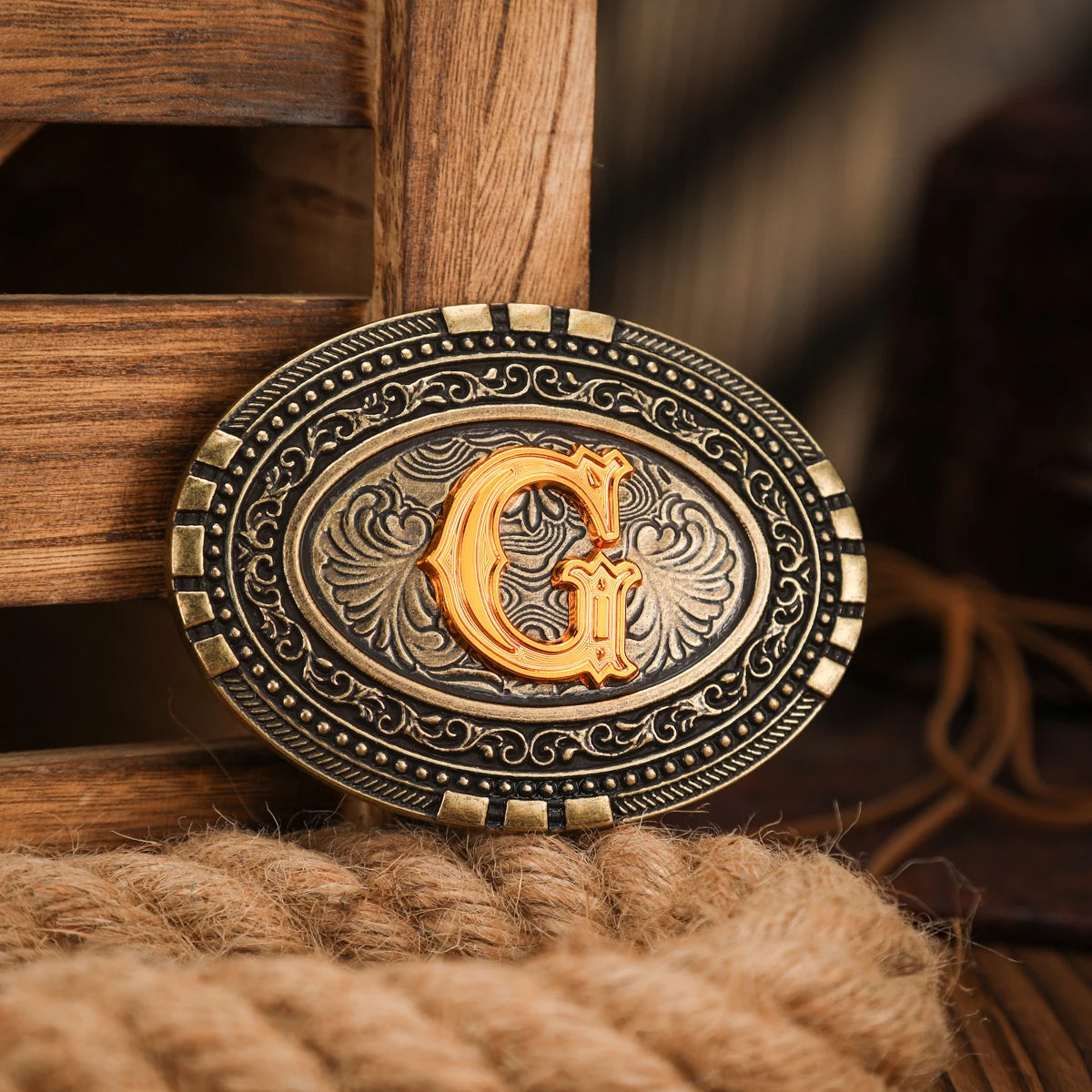 A vintage western belt buckle with an ornate gold design set in a dark metal frame, resting on a woven surface.