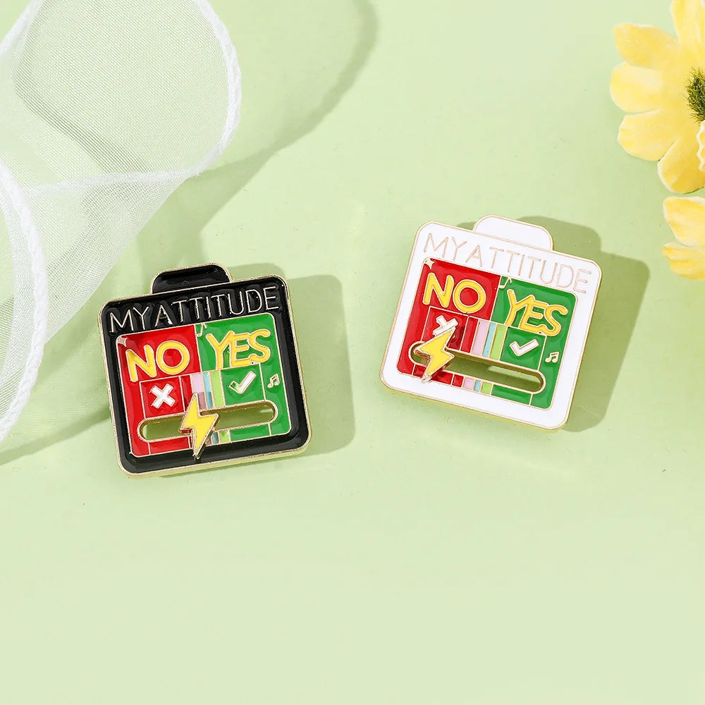 Two enamel brooch pins showing 'NO YES' and 'YES YES' mood expressions on a light green background.