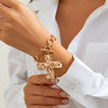 Nahaufnahme einer Hand mit einem 18k-Gold-Lagenkräuz-Anhänger an einem weißen Hemd.