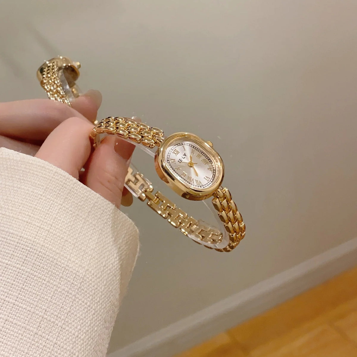 A hand is holding a gold-toned quartz fashion wristwatch with a mesh band against a light background.