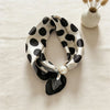 A black and white polka dot silk scarf tied with a satin knot, resting on a beige linen cloth.