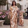 A woman models a beige and brown tropical floral leopard print abaya scarf outdoors against a white building.