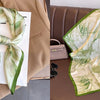A light green and gold floral print silk scarf draped on a beige blazer next to a small handbag.