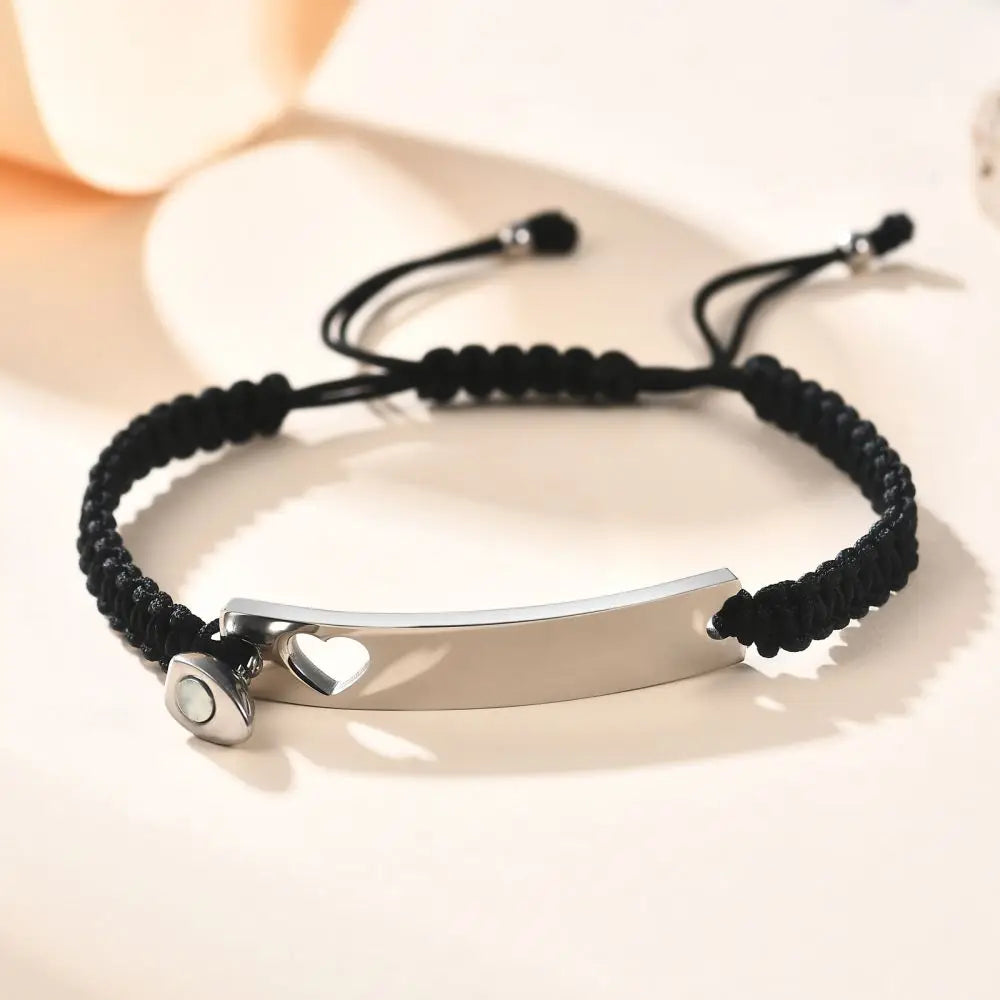 Silber-Edelstahl-Paararmband-Set mit schwarzem Schnur und Herz-Anhängern auf heller Oberfläche.