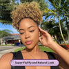 A woman with natural curly hair styled in an afro puff ponytail looking directly at the camera outdoors.
