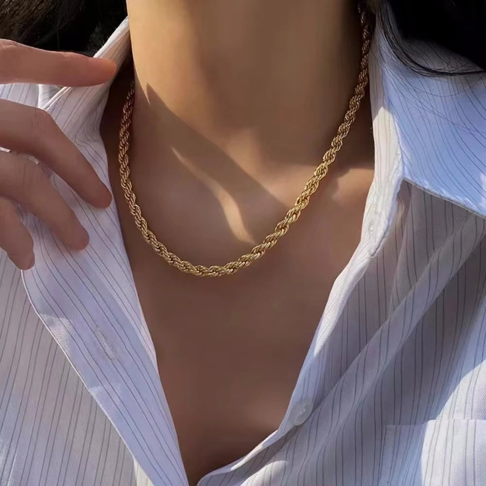 A close-up of a gold rope charm necklace worn around the neck against a white collared shirt.