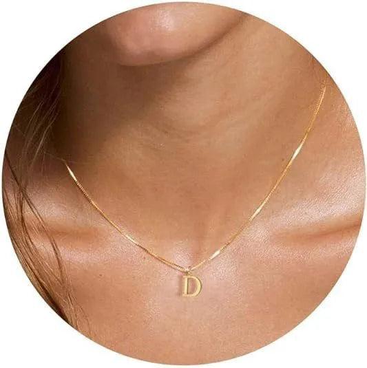 A close-up of a gold plated alphabet initial necklace resting on the skin of a person's neck.