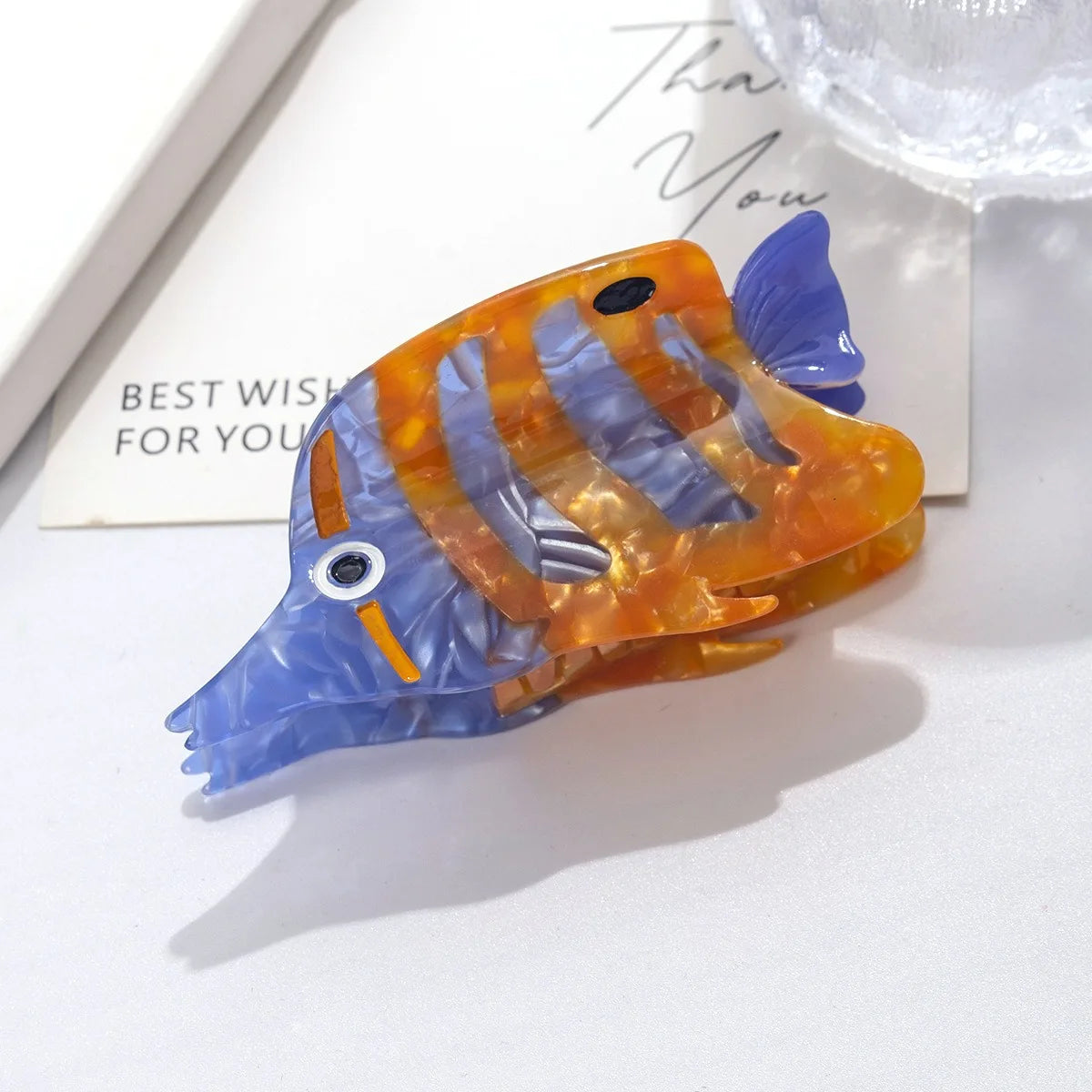 Pinza para el pelo con forma de pez y escamas azules y naranjas.