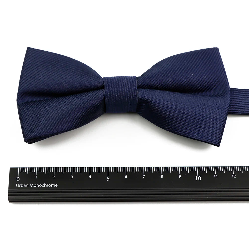 Navy blue bow tie and suspenders set with a ribbed texture displayed above a ruler.
