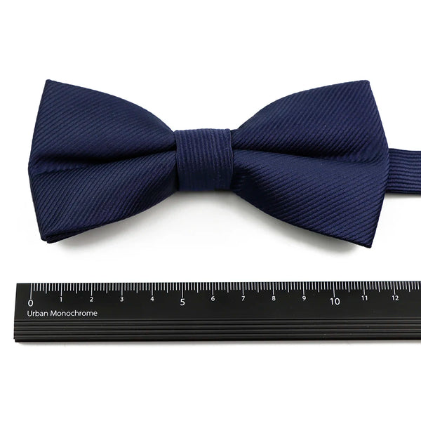 Navy blue bow tie and suspenders set with a ribbed texture displayed above a ruler.