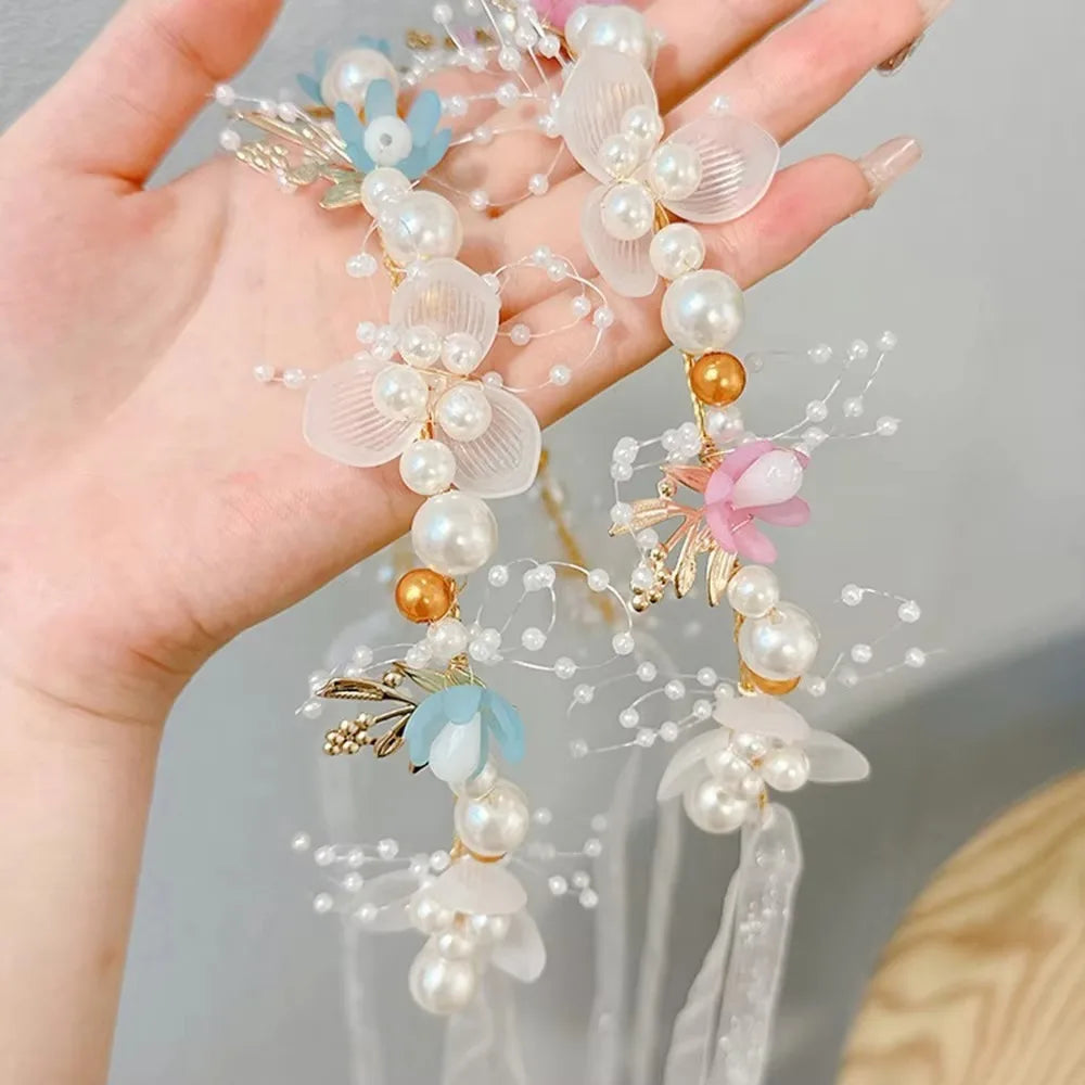 A delicate floral wreath headband made of pearl and sheer fabric is held in a hand.