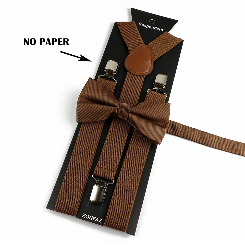 A set of brown polyester suspenders with bow ties and a leather suspender holder on a black card.