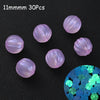 Thirty 11mm luminous glow-in-the-dark acrylic beads scattered on a dark surface with a close-up of blue and green glowing bea