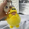 A yellow fluffy cartoon plush doll keychain with a silver charm is held in a hand.