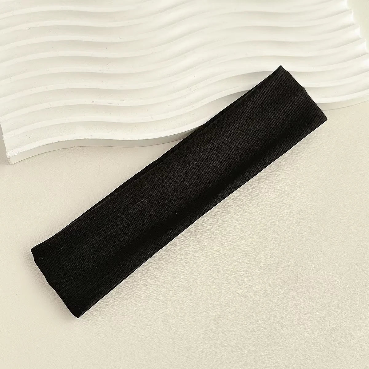 A black fabric headband is shown diagonally against a white, wavy background.