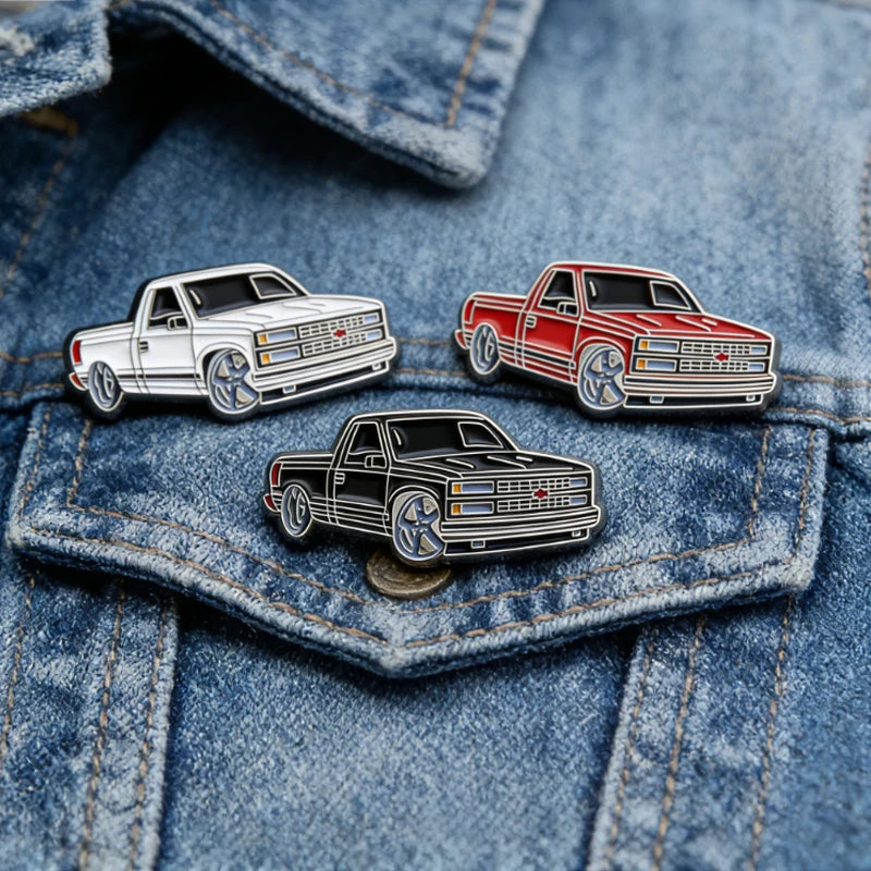 Three metal clip pins featuring classic pickup trucks in silver, red, and black on a denim shirt.