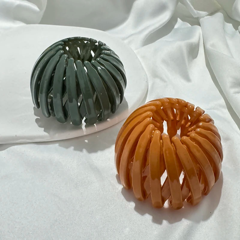 A pair of elegant, spiral-shaped hair clips in dark green and amber tones resting on a white surface.