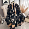 A black and beige plaid cashmere scarf and shawl wrap draped over a white chair.