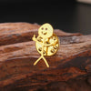 A gold punk stickman brooch shaped like a smiling figure with arms raised, resting on dark brown rock.