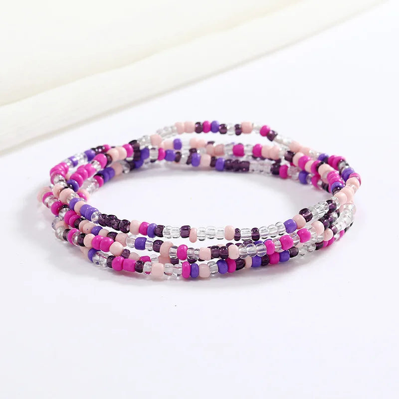 Una pulsera hecha de cuentas de colores en tonos rosa, púrpura y blanco, mostrada sobre un fondo blanco.
