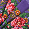 A close-up of a purple silk scarf featuring a vibrant floral print with red, orange, and green leaves.