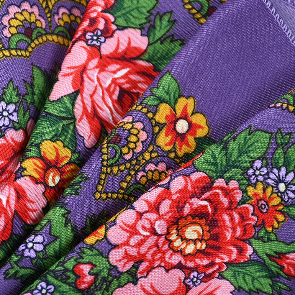A close-up of a purple silk scarf featuring a vibrant floral print with red, orange, and green leaves.