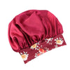 A deep maroon satin sleep bonnet with a gathered top and an elastic band featuring a floral print.