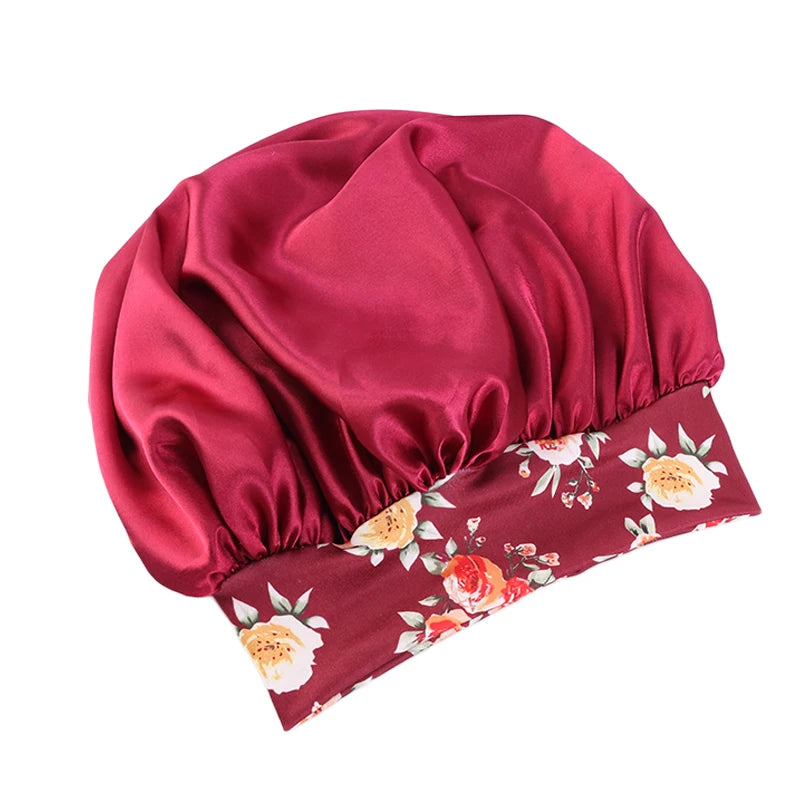 A deep maroon satin sleep bonnet with a gathered top and an elastic band featuring a floral print.