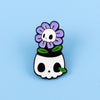 An enamel pin featuring a purple flower skull design with green leaves.