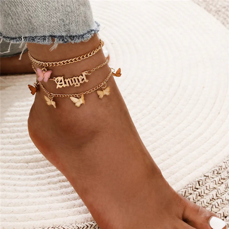 Goldenes Vintage-Schmetterlingsherz-Armband-Set, getragen am Fuß vor weißem, strukturiertem Hintergrund.